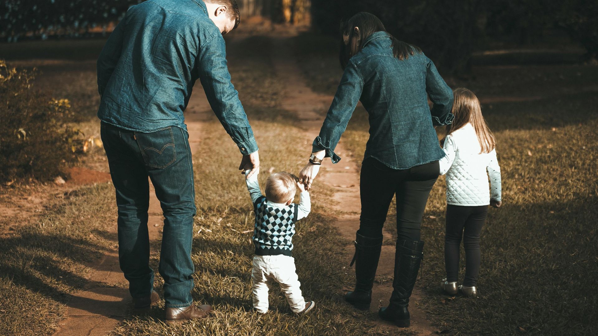 A family of four walks hand in hand on a path, enjoying a sunny day outdoors.