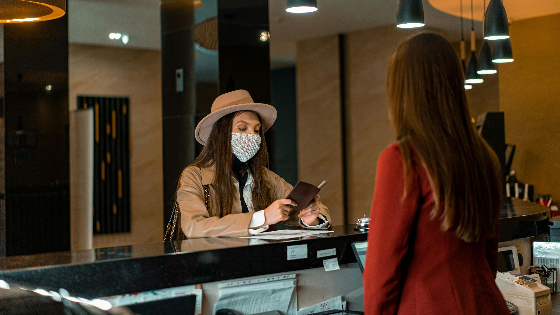 A woman wearing a mask checks in at a hotel reception desk.