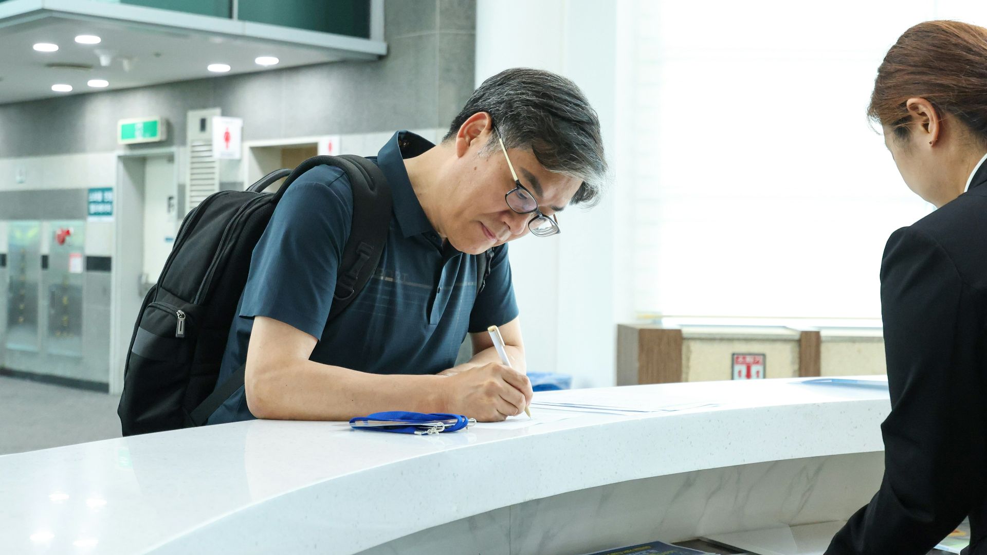 A man signs paperwork at a reception desk.