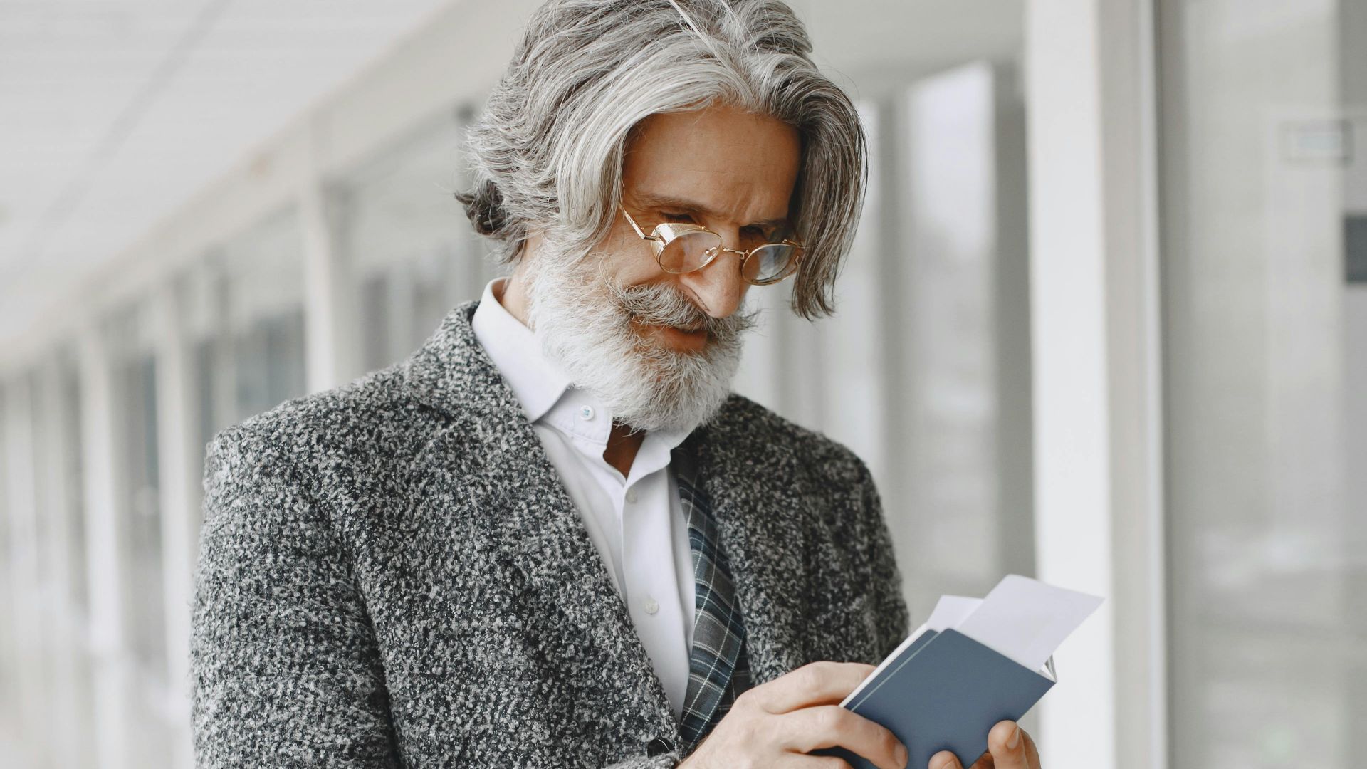 Elegant senior businessman in a suit holding a passport indoors.