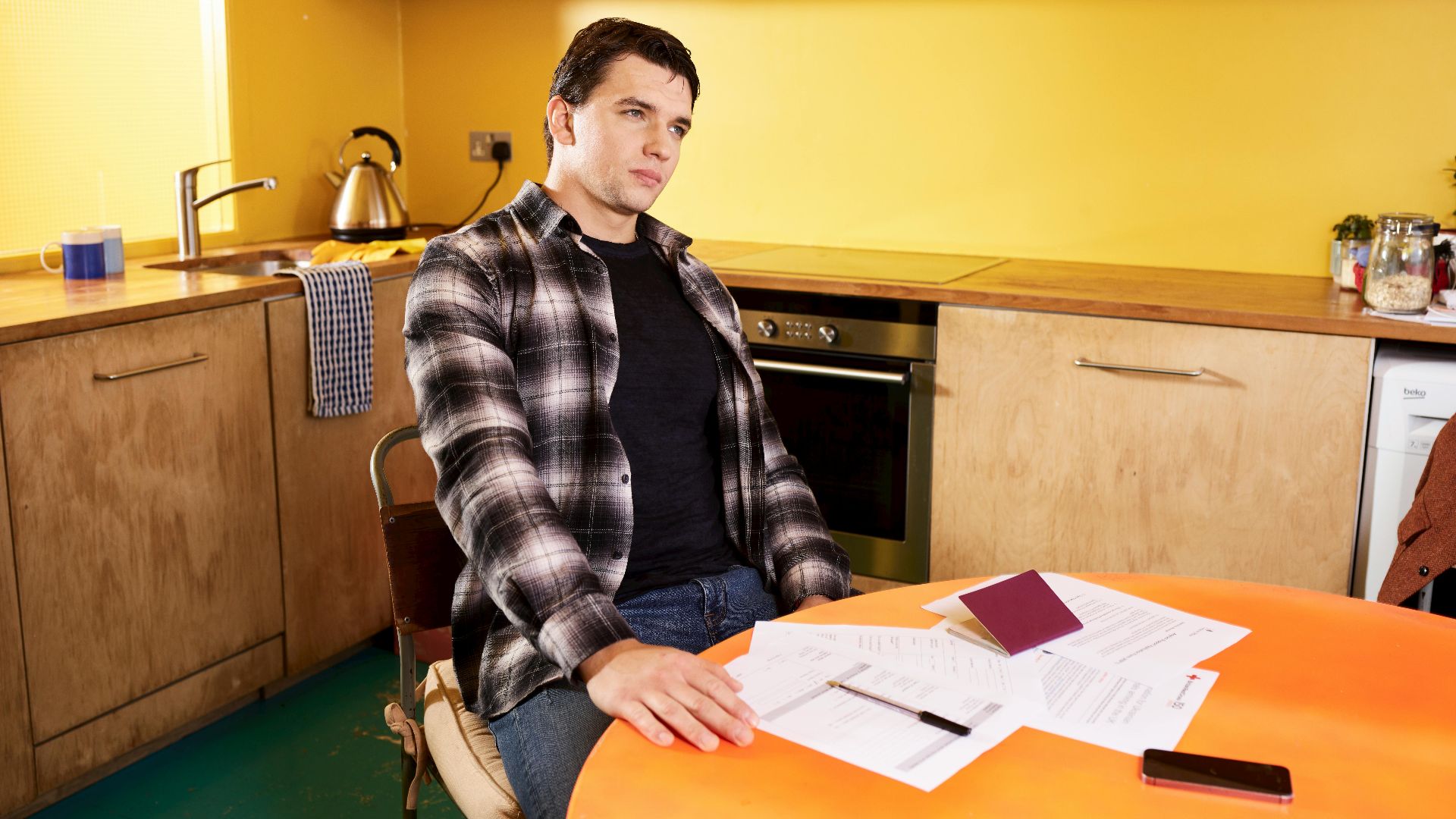 Man sitting at a kitchen table with documents and a passport, contemplating.