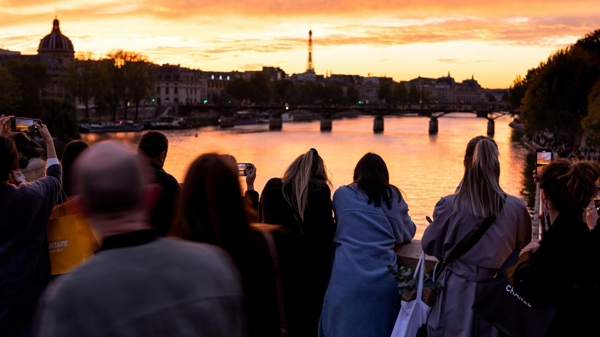 Crowd enjoying a vibrant sunset over the Seine in Paris, featuring the Eiffel Tower.