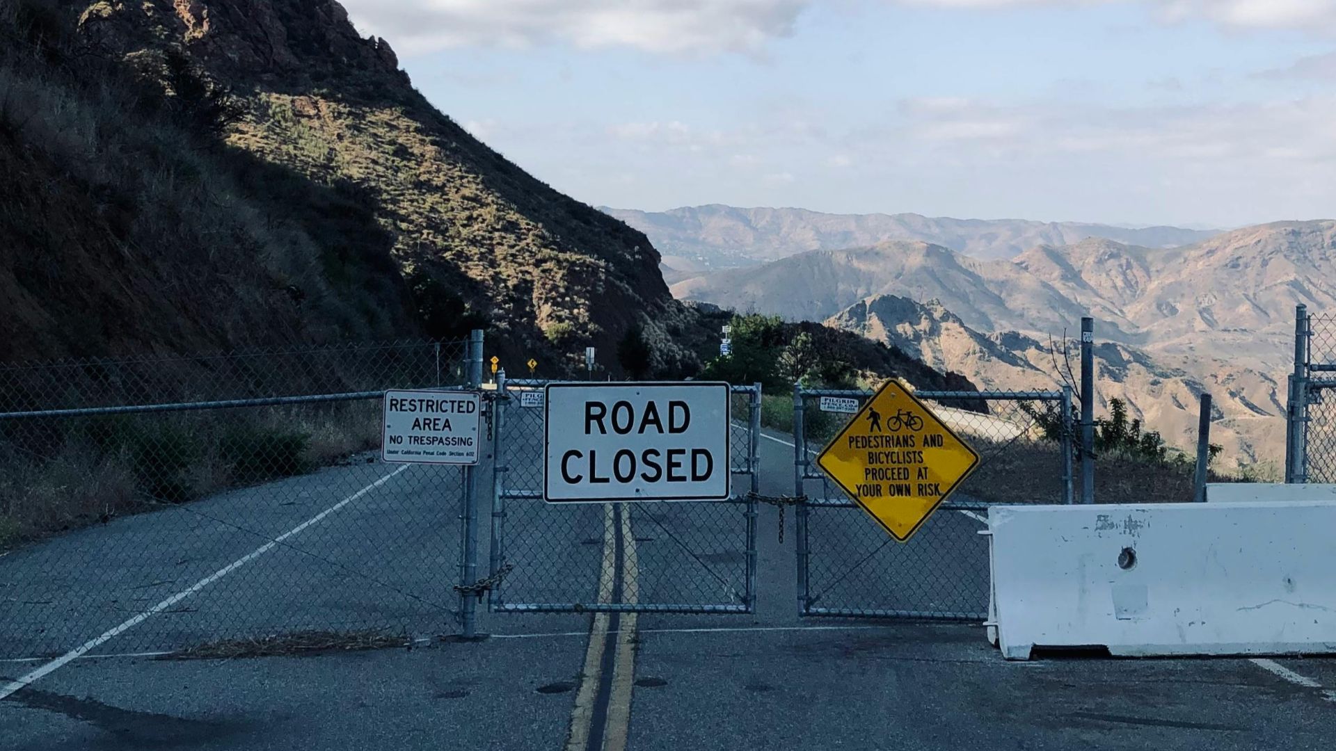 A metal gate blocks a mountain road with scenic views in the background.