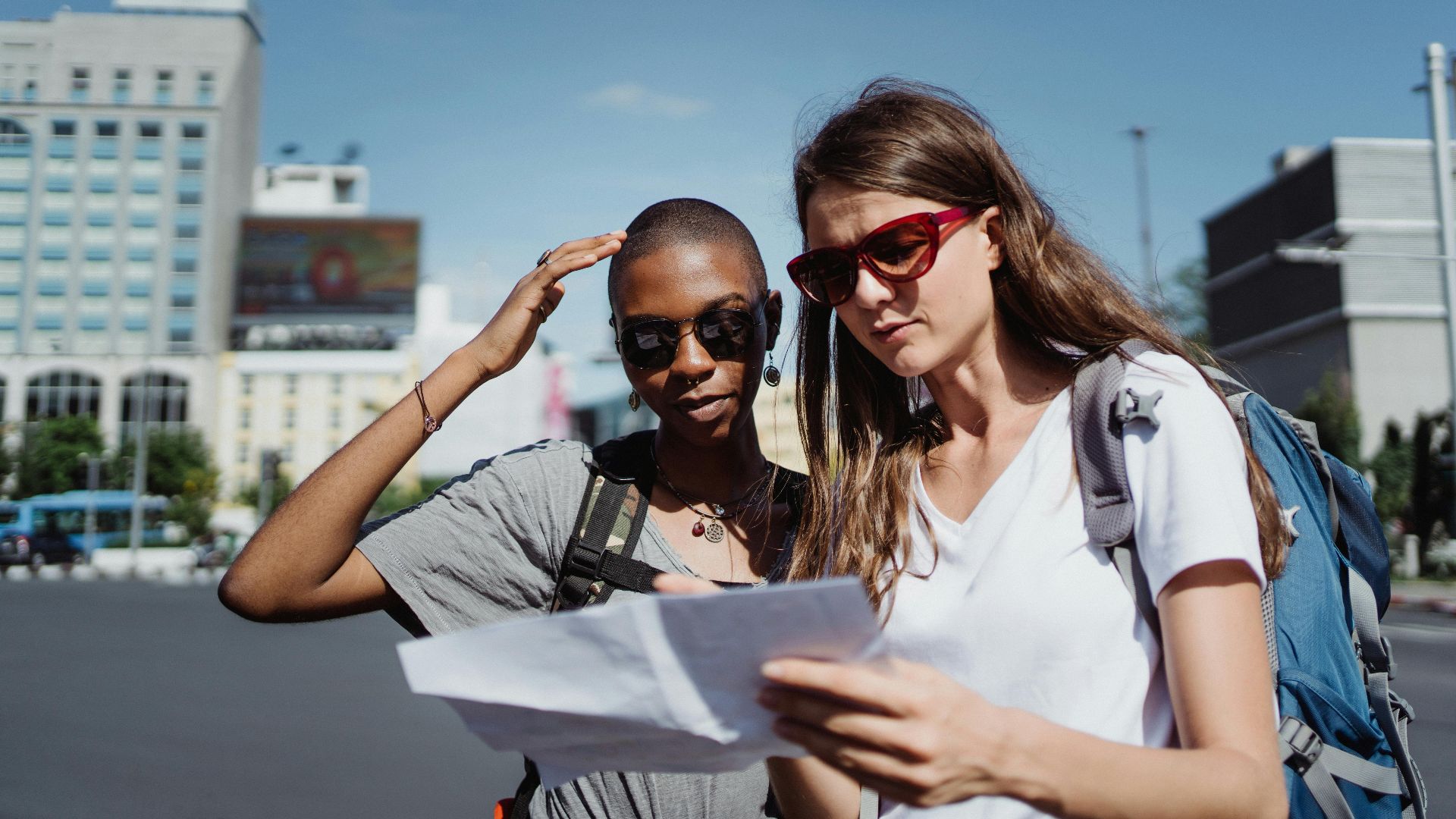 Two women tourists checking a map while exploring a city on a sunny day.