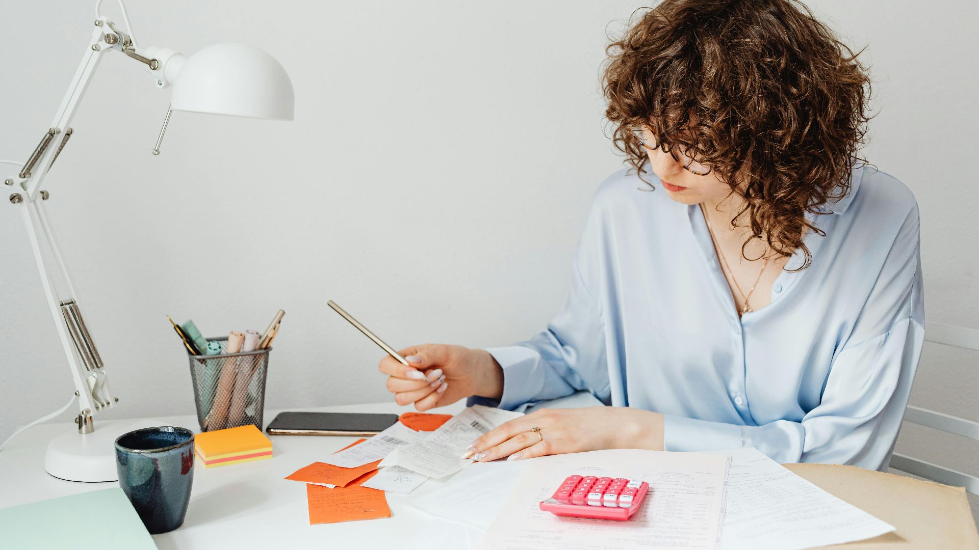Woman in office calculating expenses with documents, calculator, and coffee.