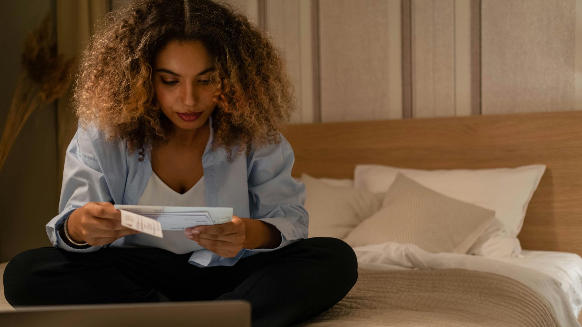 Woman sitting on bed reading documents with laptop, highlighting home office setting.