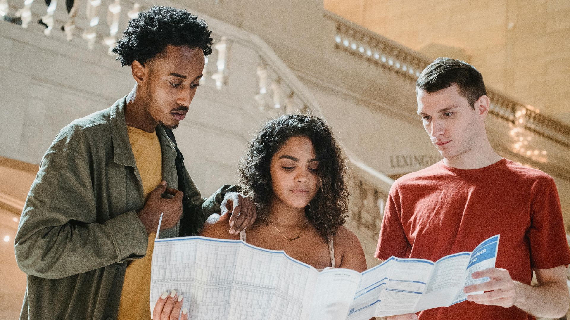 Low angle of concentrated young multiracial students reading map while searching for route in Grand Central Station in New York