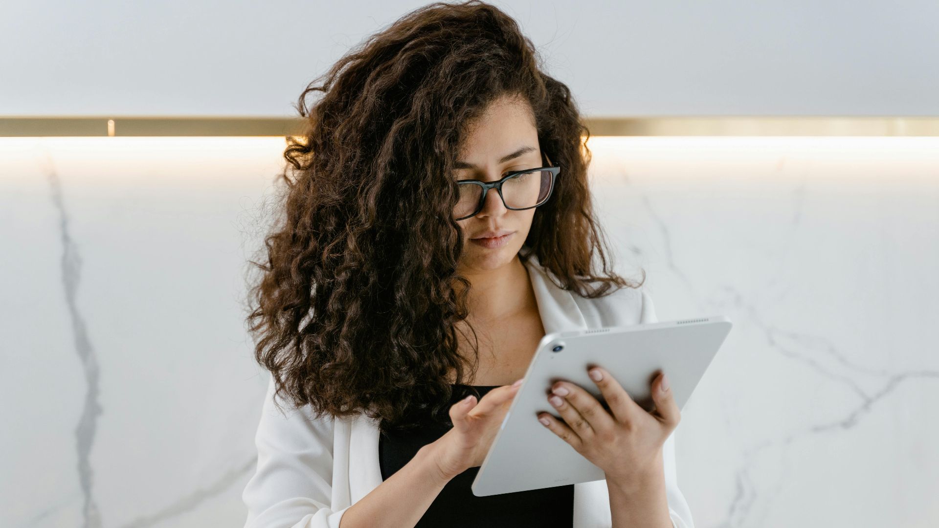 A woman uses a tablet in a modern kitchen, focusing on technology and multitasking.