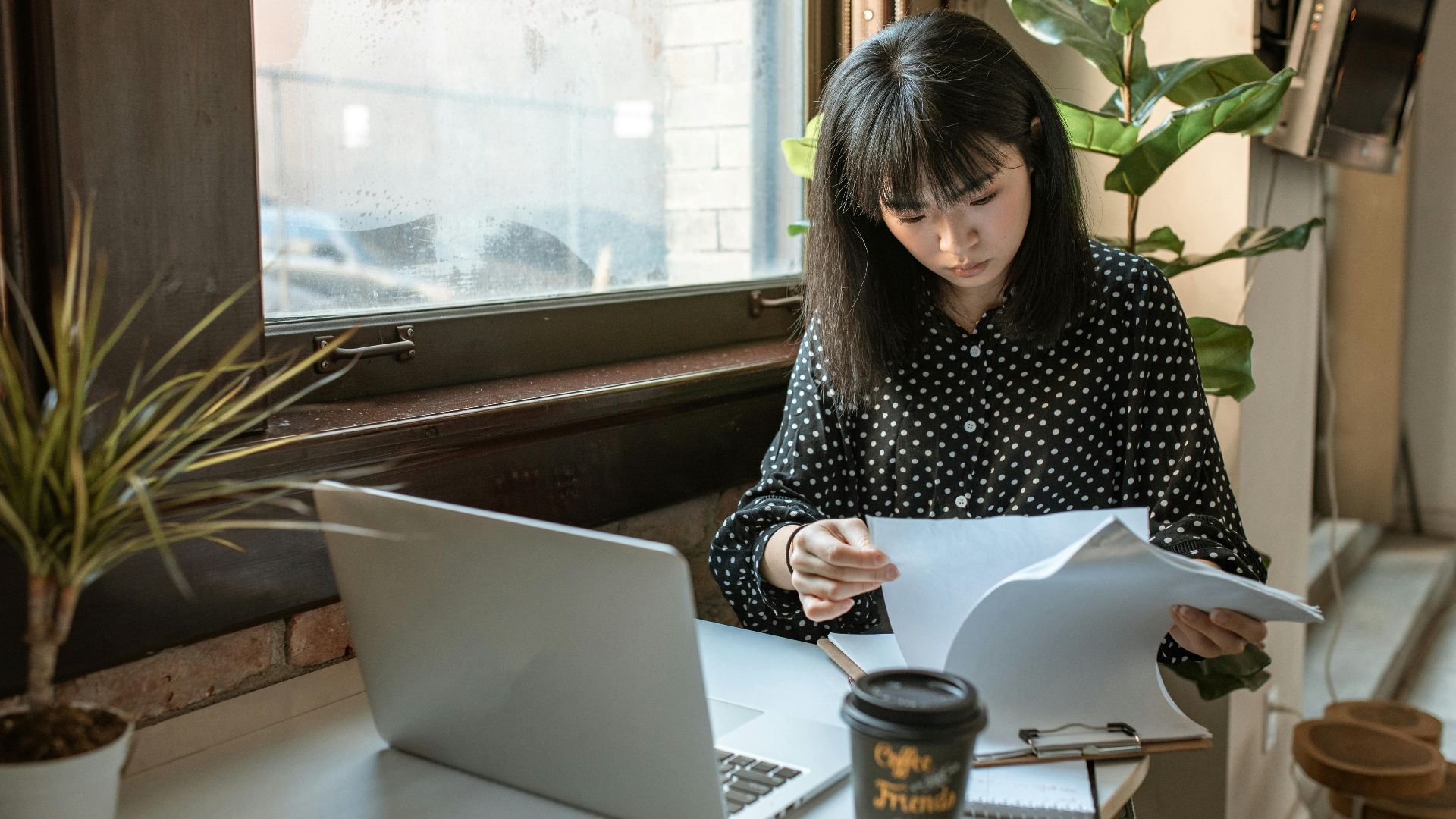 Asian businesswoman reviewing documents in a modern office setting with natural light.