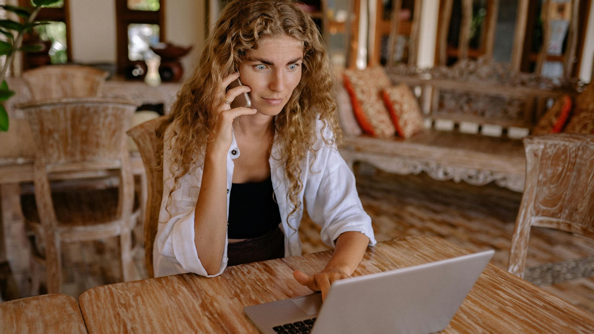 Woman working remotely on a laptop while talking on phone, capturing freelance lifestyle.