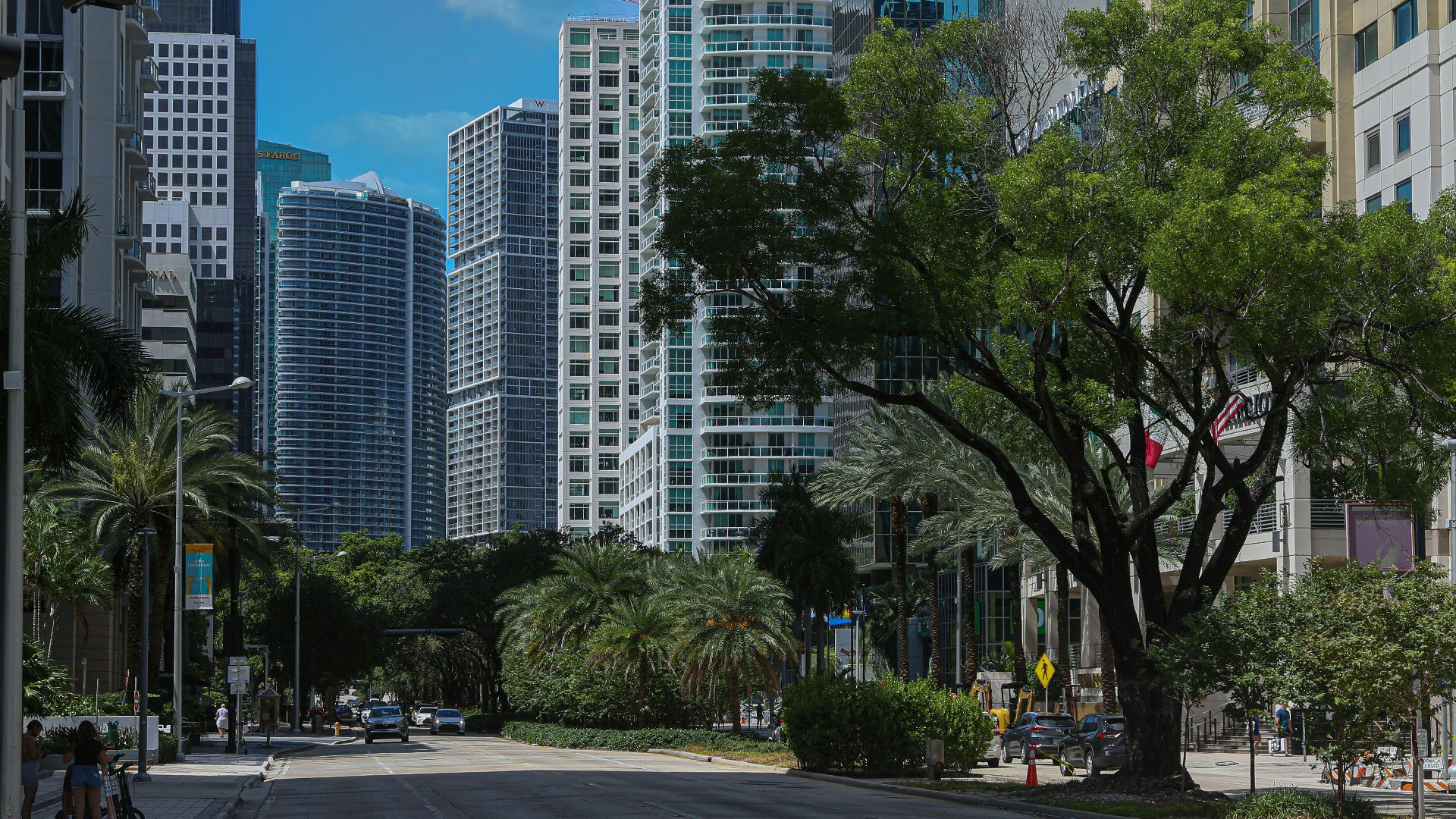 Lively street in downtown Miami featuring skyscrapers and lush palm trees under a bright blue sky.