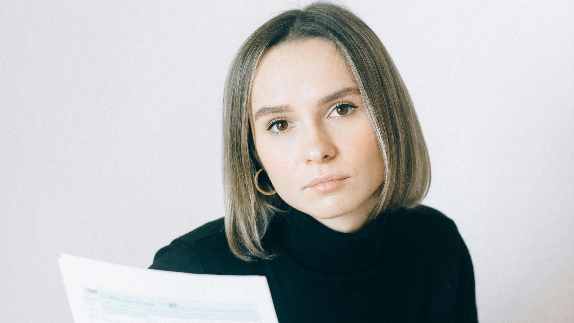 Caucasian woman in black sweater reviewing documents at a desk with paperwork and a laptop.