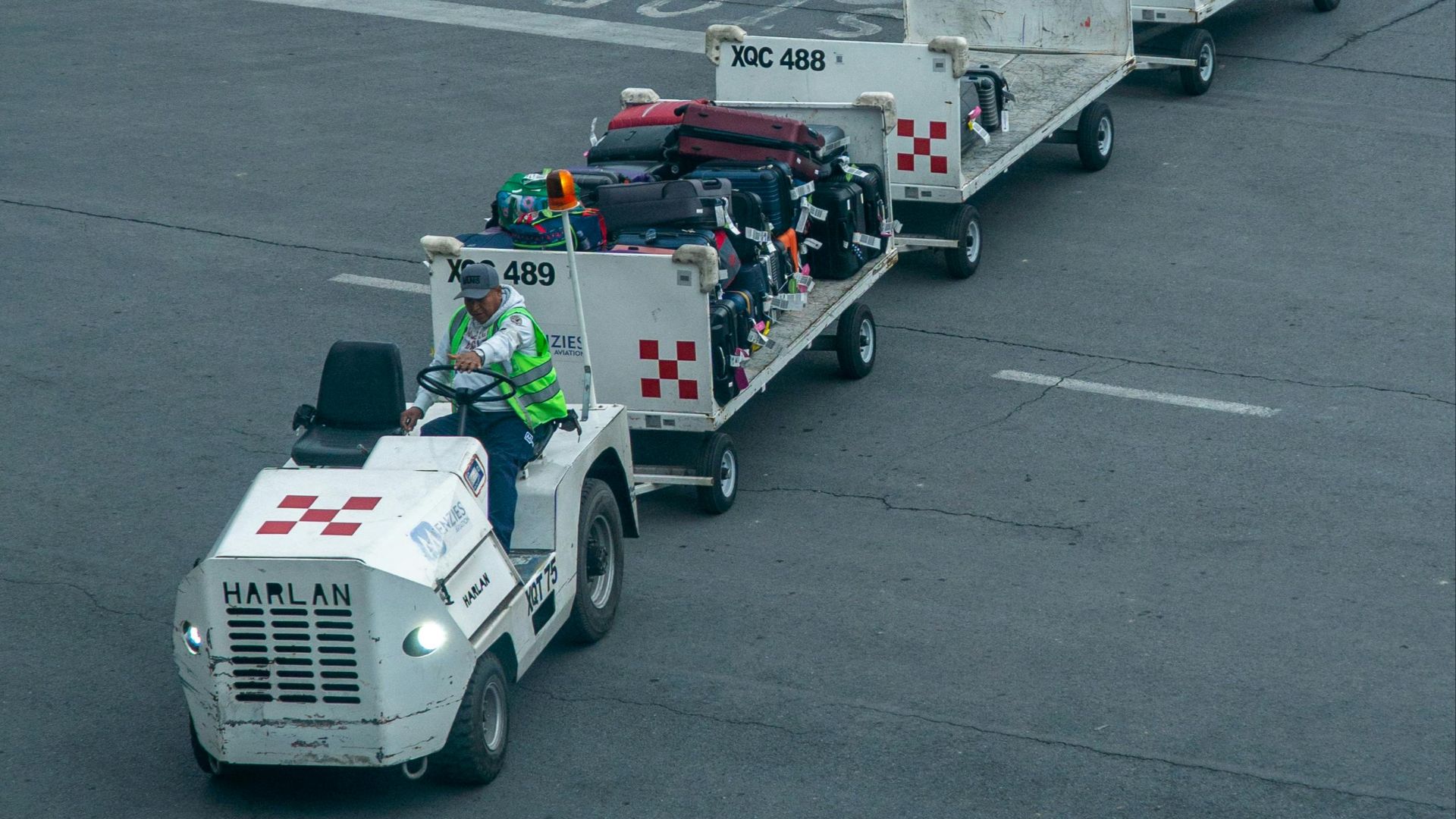 Ground crew managing luggage on tarmac with baggage carts and vehicle at airport.
