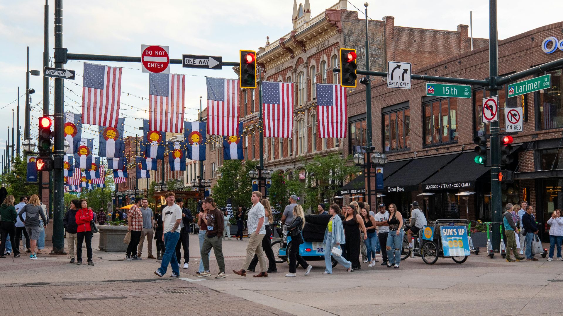 People crossing a lively intersection adorned with flags in downtown Denver.