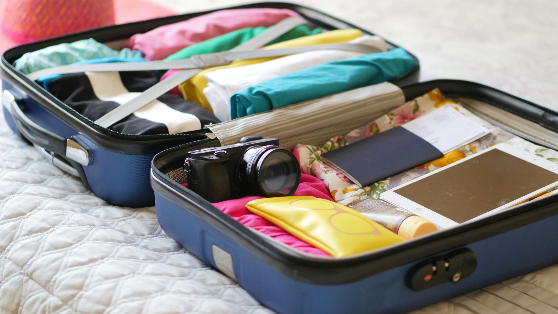 Open suitcase with camera, clothes, and passport, ready for a summer vacation.