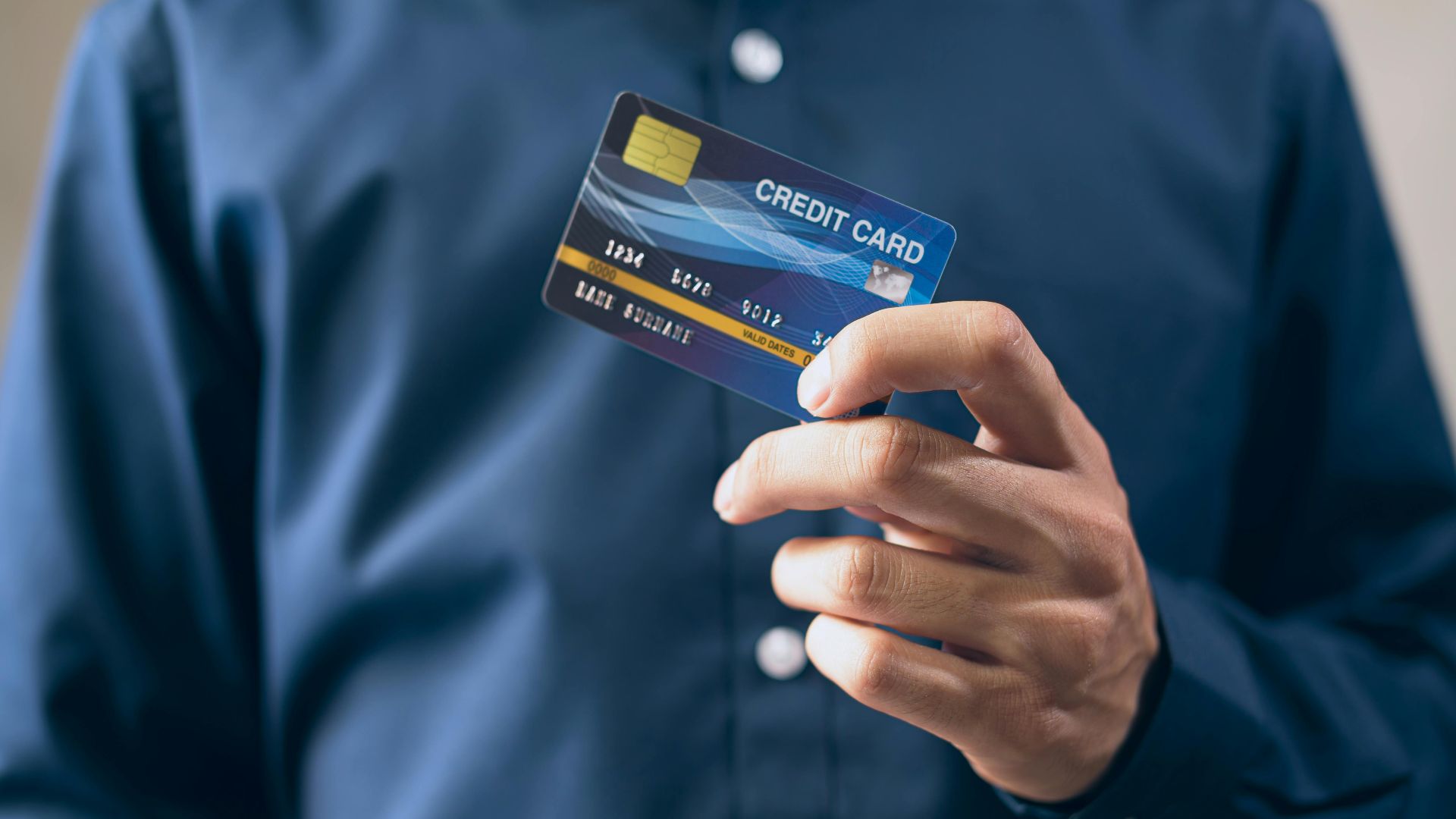 Close-up of a person holding a credit card in a hand, wearing a button-up shirt.