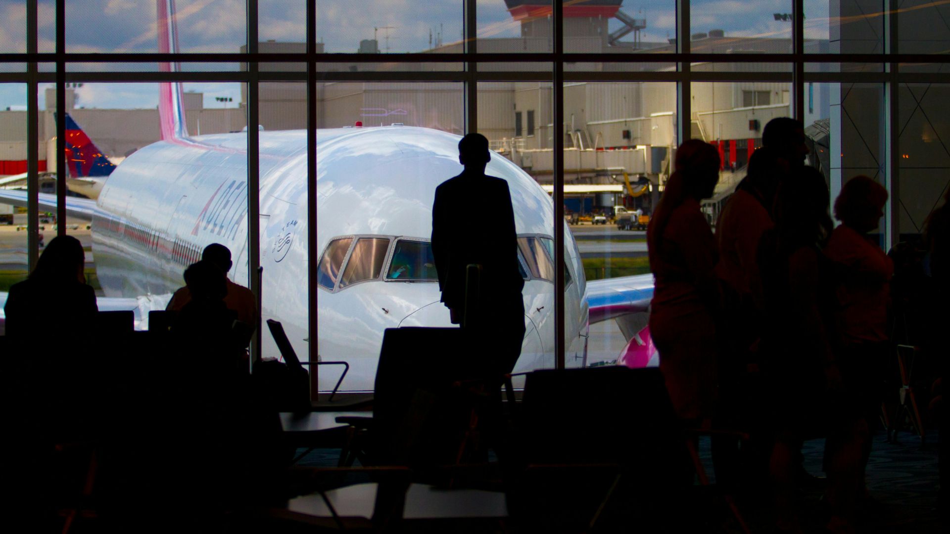 Silhouettes of travelers waiting at an airport terminal with an airplane visible through the window.