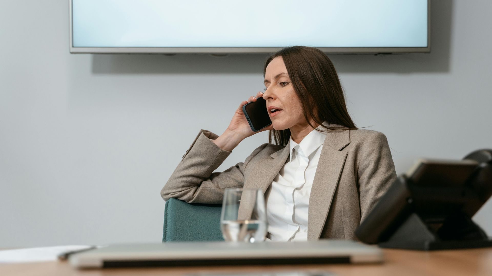 Businesswoman in a blazer making a phone call in an office setting, engaging in a conversation.