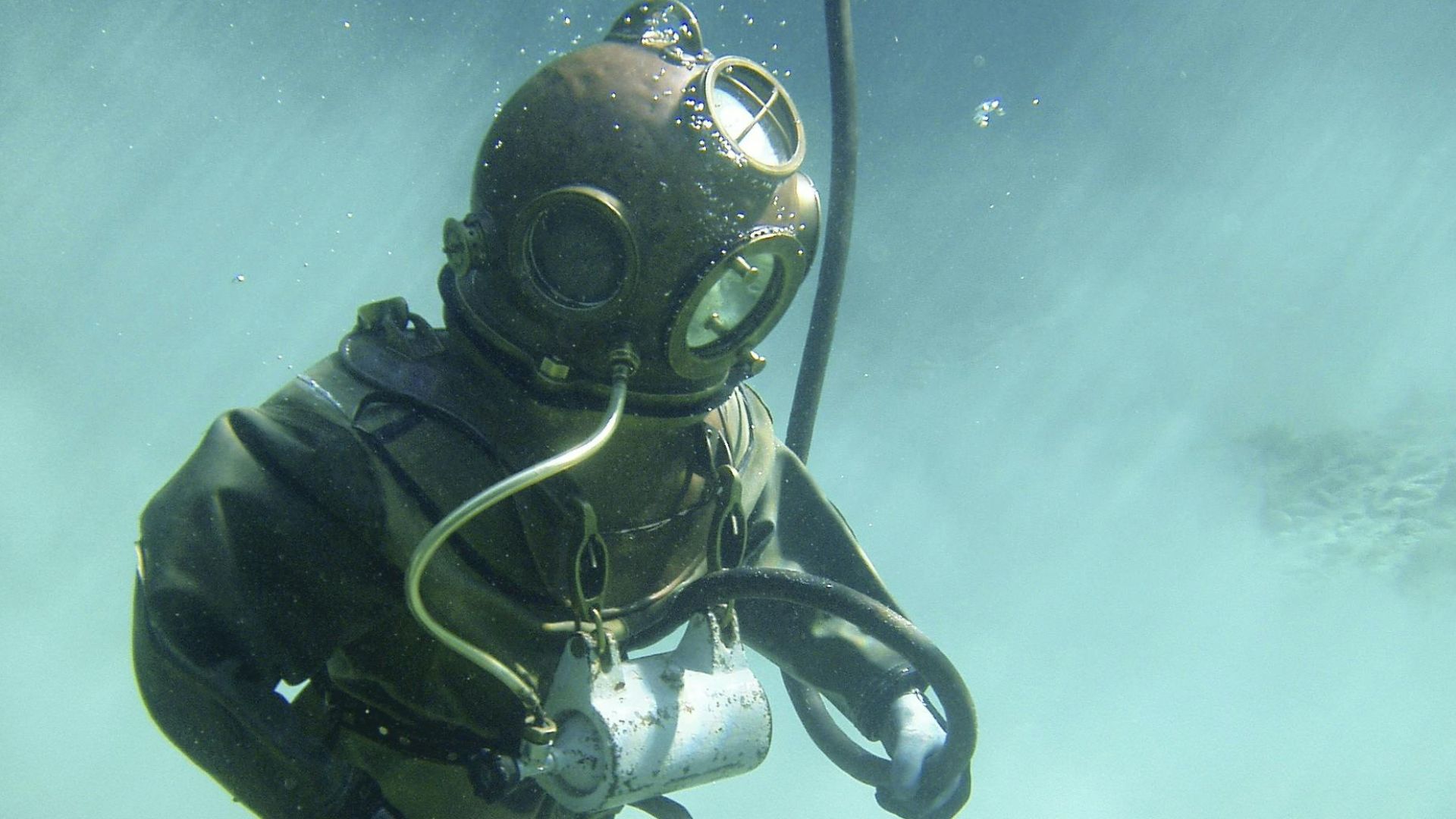 A vintage diver in a classic suit explores underwater, surrounded by clouds of sand.