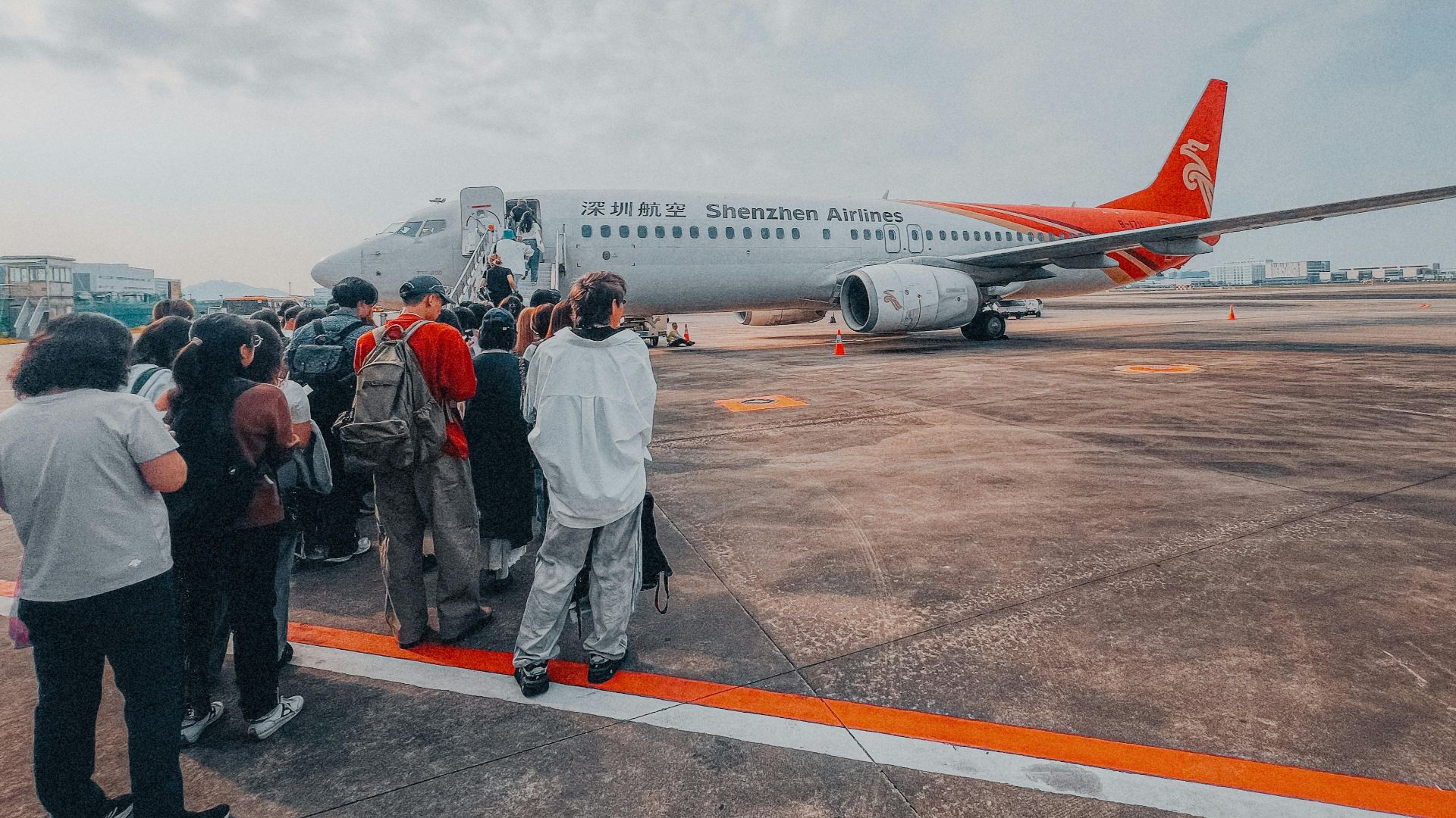 Passengers line up to board a Shenzhen Airlines aircraft on a cloudy day. Travel and adventure await.