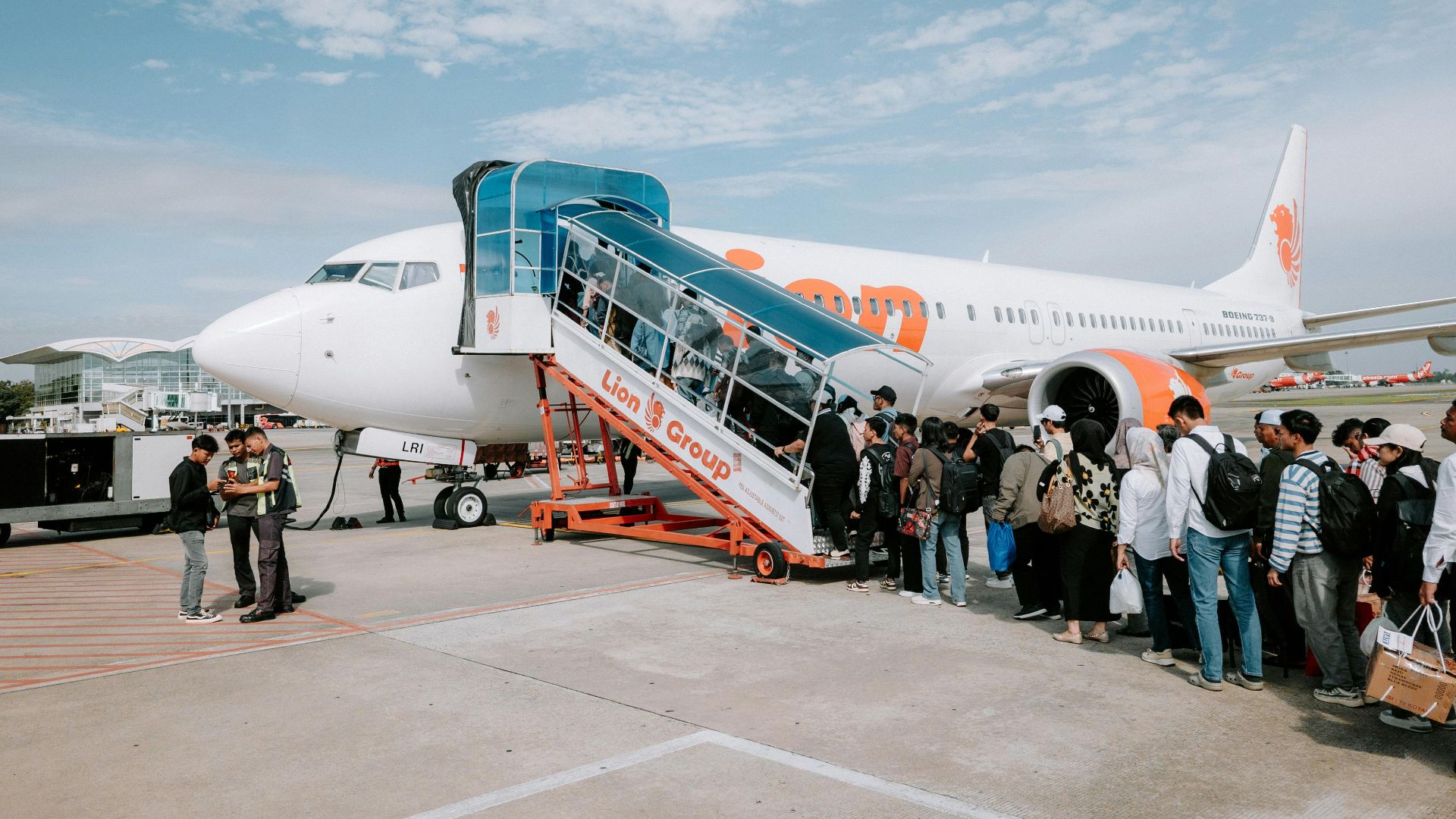 Travelers line up to board a Lion Air airplane at Medan Airport, Indonesia, during a sunny day.