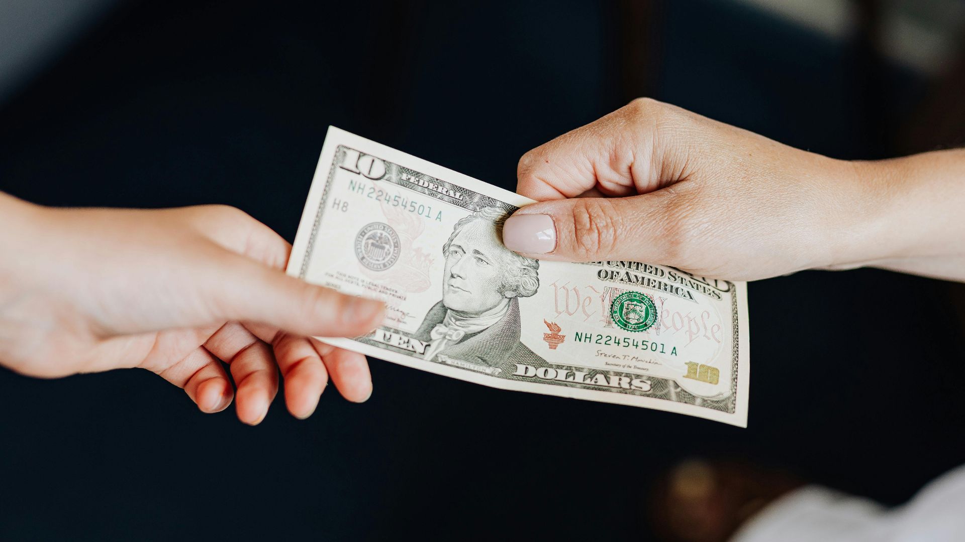 Two people exchanging a ten dollar bill in a close-up hand-to-hand transaction.