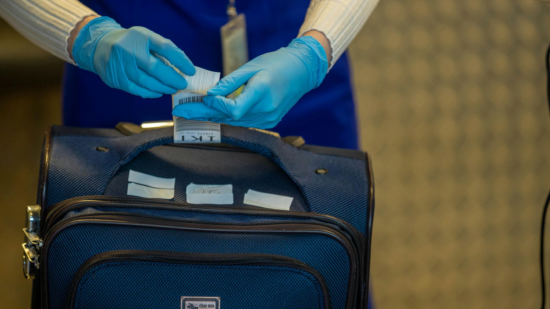 Close-up of airport security process with gloved hands inspecting luggage tags.