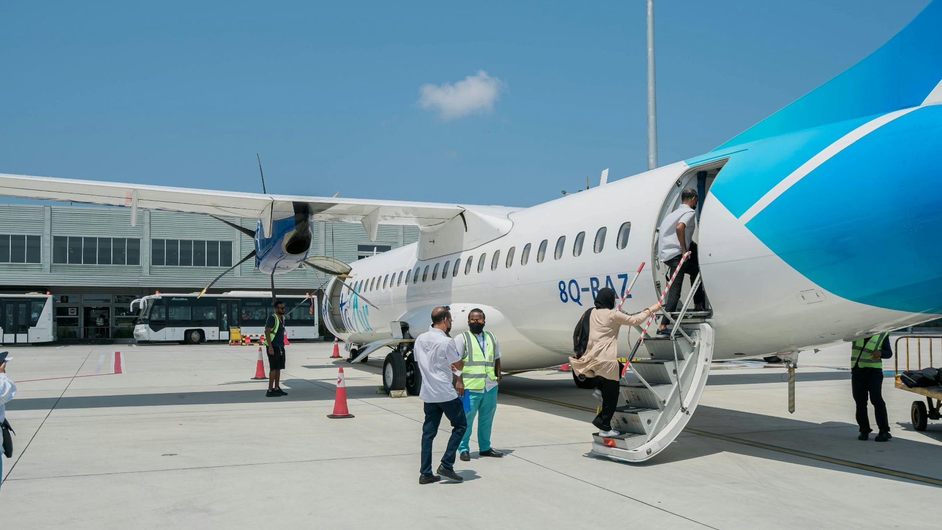 Passengers board a blue and white ATR 72 aircraft at an airport under clear skies.