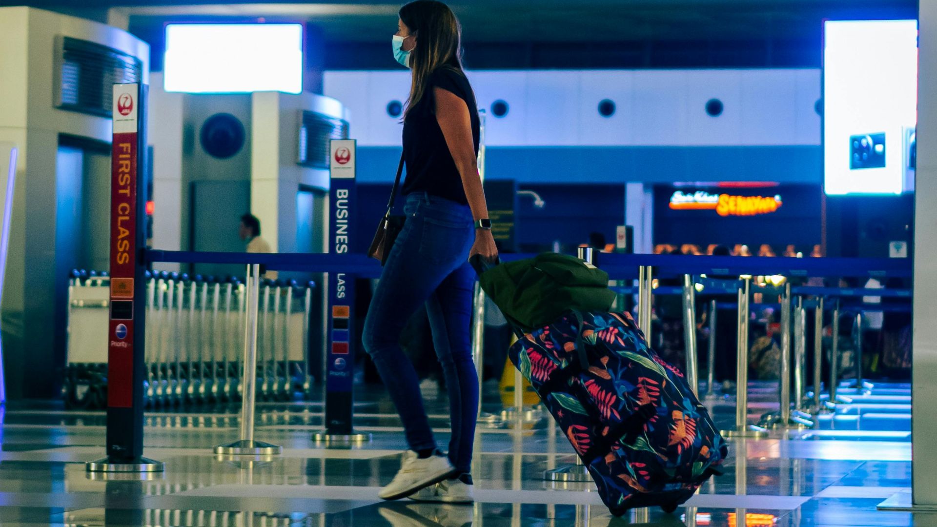 A woman wearing a face mask walks through an airport with luggage, reflecting modern travel trends.