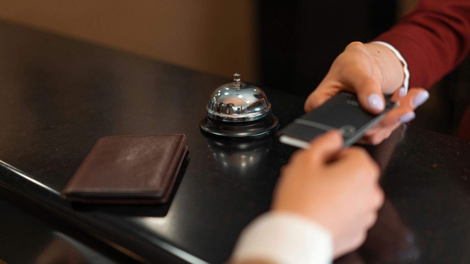 A close-up of a hotel check-in process with a smartphone and card transaction at the reception desk.