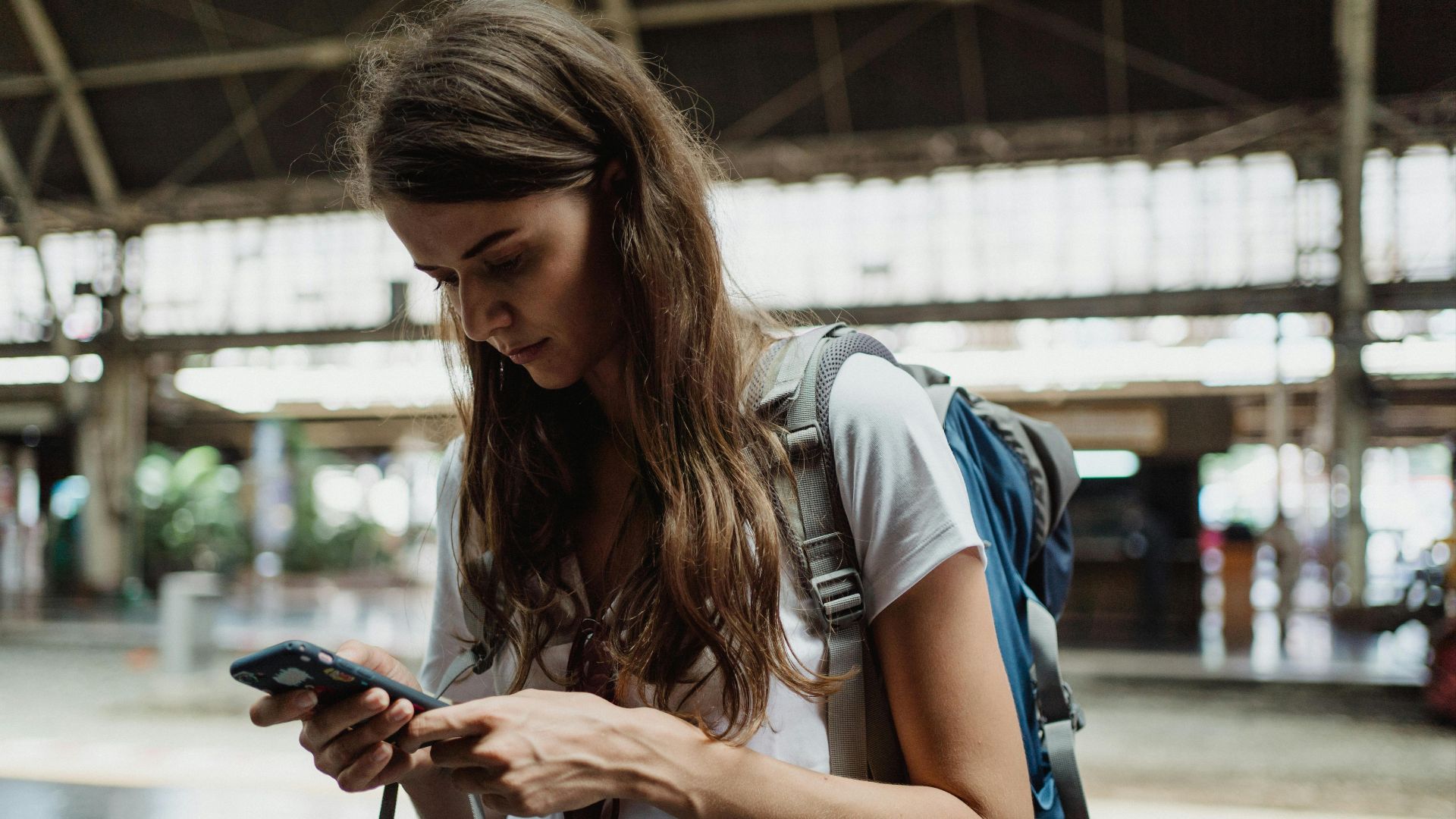A young woman checks her smartphone while traveling at a train station.