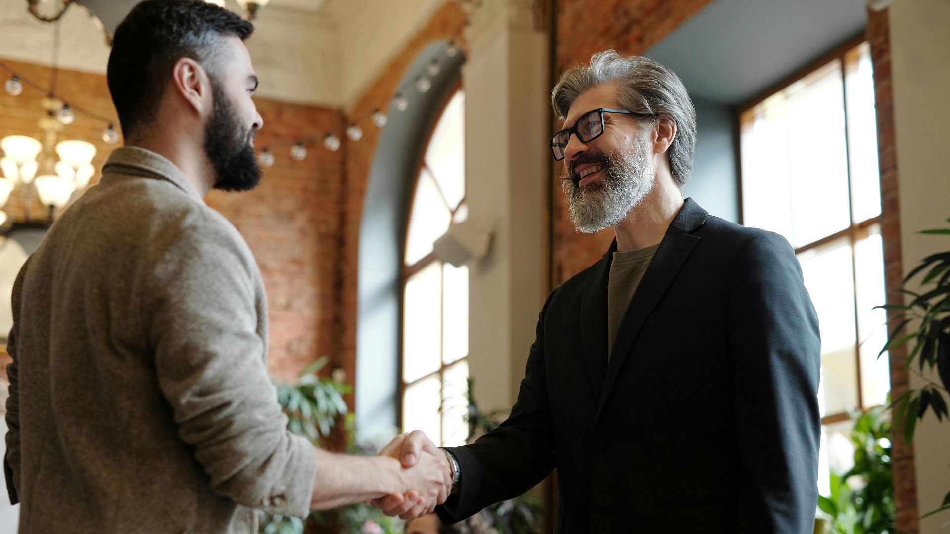 Two businessmen smiling during a handshake in a modern office setting, symbolizing success and partnership.