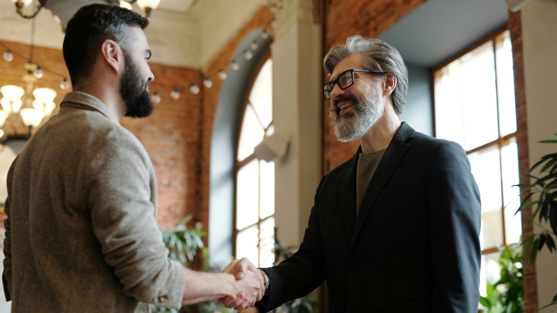 Two businessmen smiling during a handshake in a modern office setting, symbolizing success and partnership.