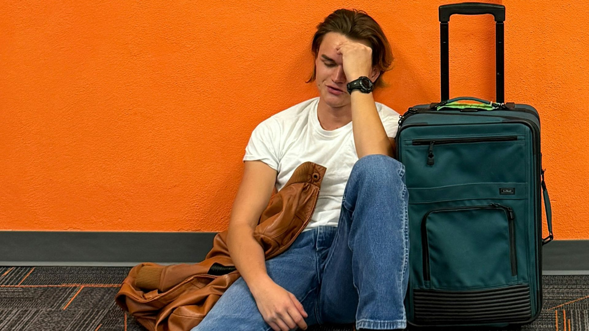 Man sitting on floor with luggage, looking tired.