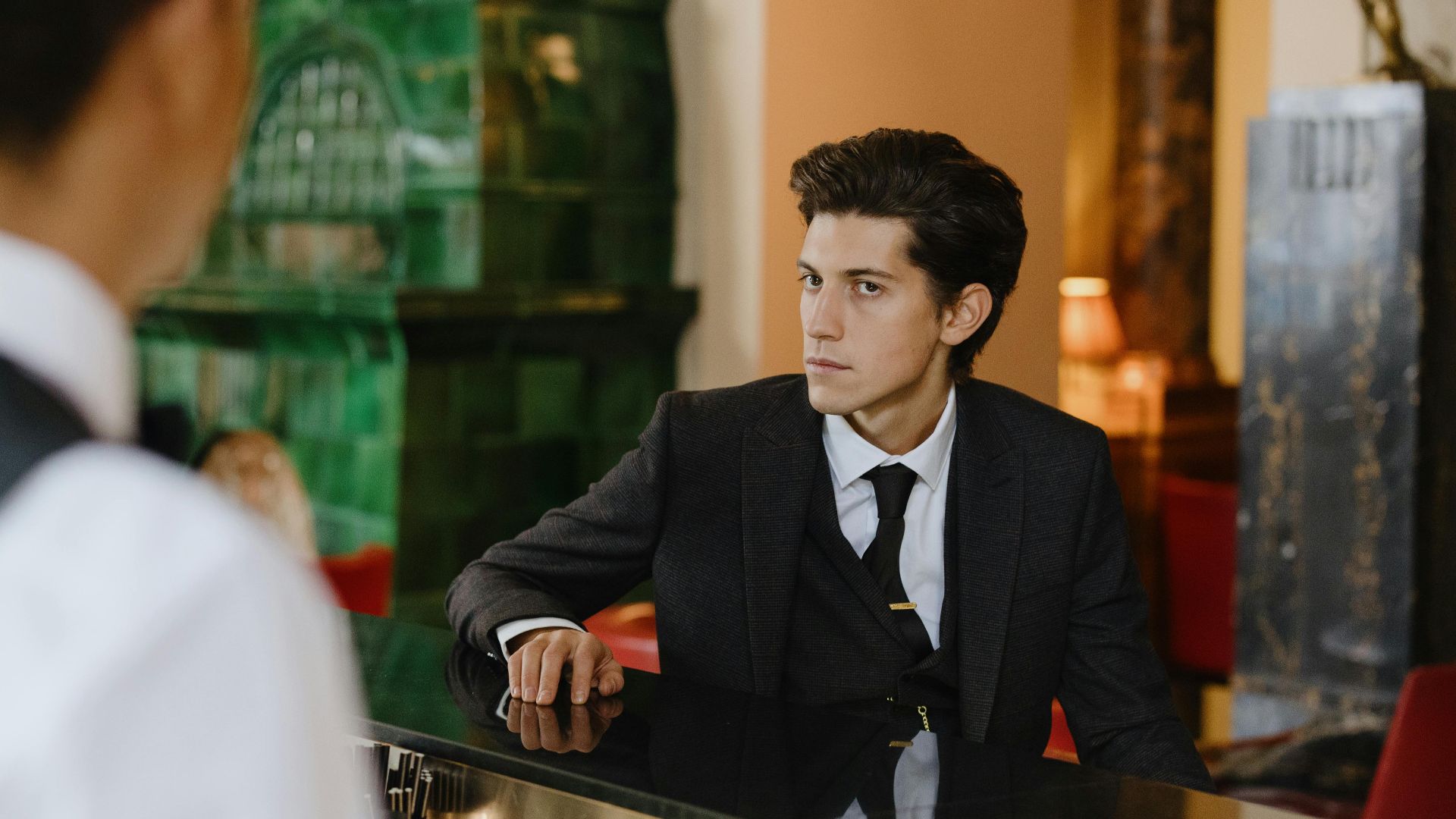 Sophisticated man in a suit sitting at a vintage bar counter indoors, exuding elegance and style.