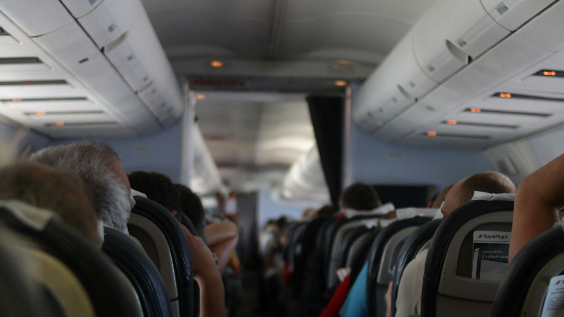 View from the back of an airplane cabin with passengers seated, showcasing travel atmosphere.