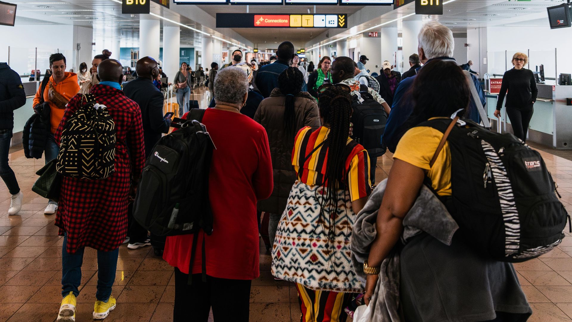 Travelers lining up in a busy airport terminal with baggage under flight information screens.