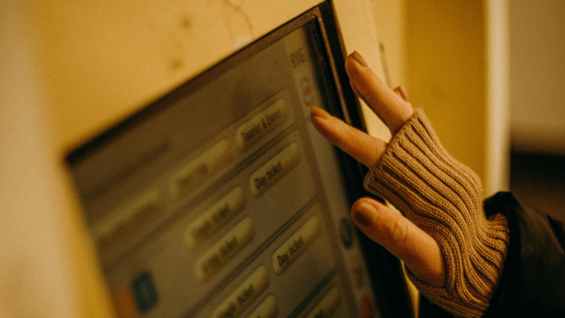 A close-up image of a gloved hand operating a Berlin U-Bahn ticket machine showing electronic interface and selection buttons.