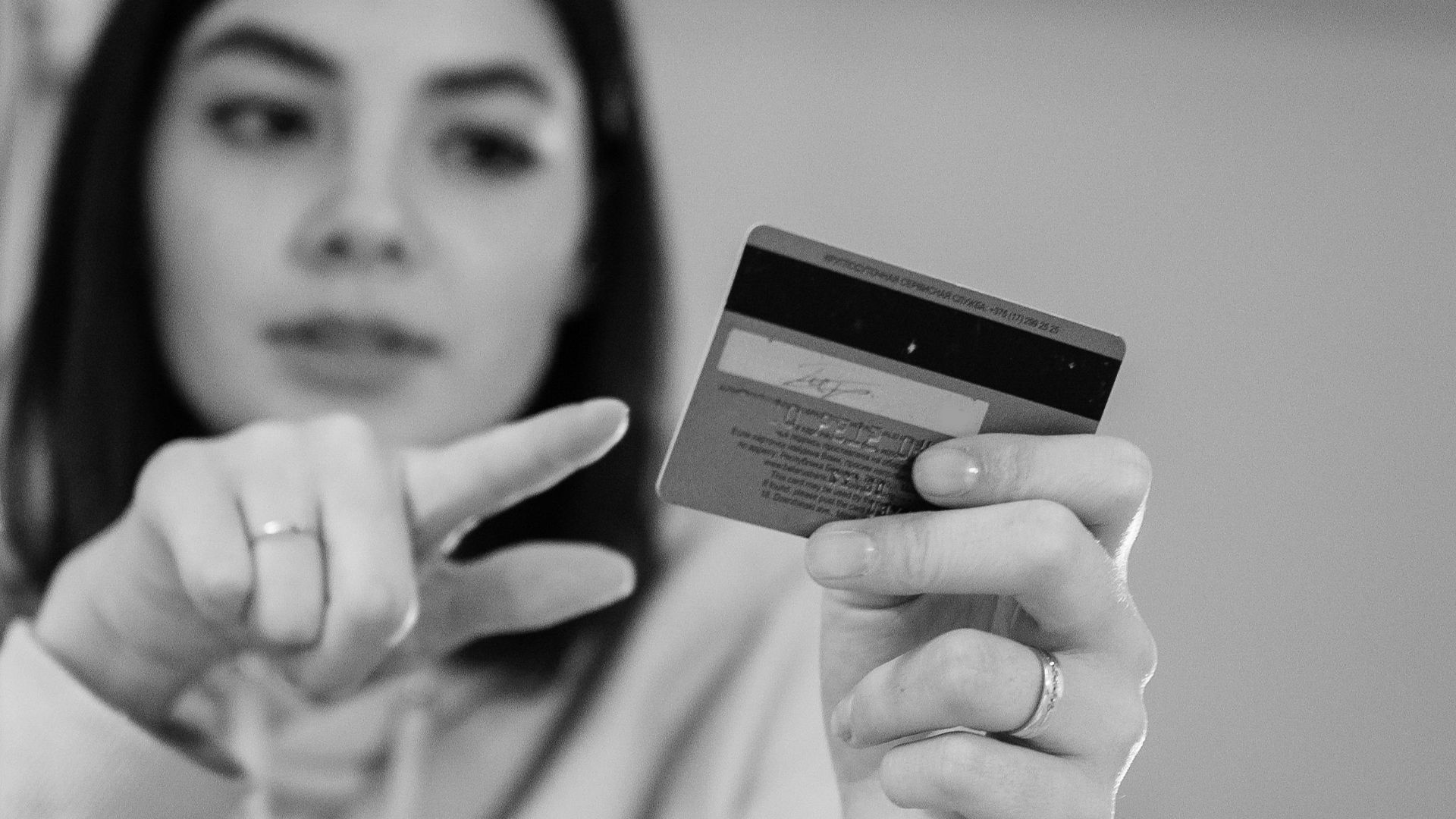 Black-and-white image of a woman pointing at a credit card indoors.