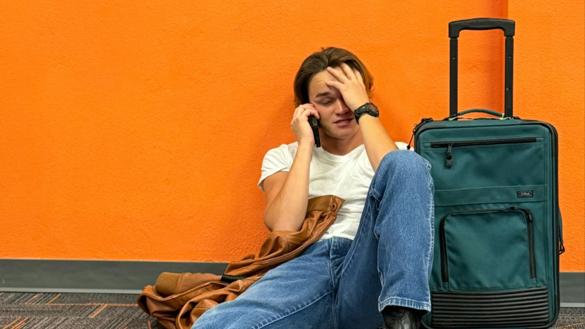Man sitting on floor with suitcase, looking distressed.