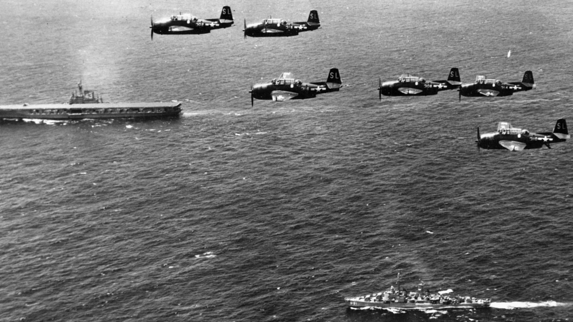 Six U.S. Navy Grumman TBM-3E Avenger anti-submarine aircraft of Composite Squadron VC-22 Checkmates flying over the Mediterranean Sea. This squadron was Attack Squadron VA-2E until 4 August 1948. Below are the aircraft carrier USS Coral Sea (CVB-43) and the Gearing-class destroyer USS Bordelon (DD-881).