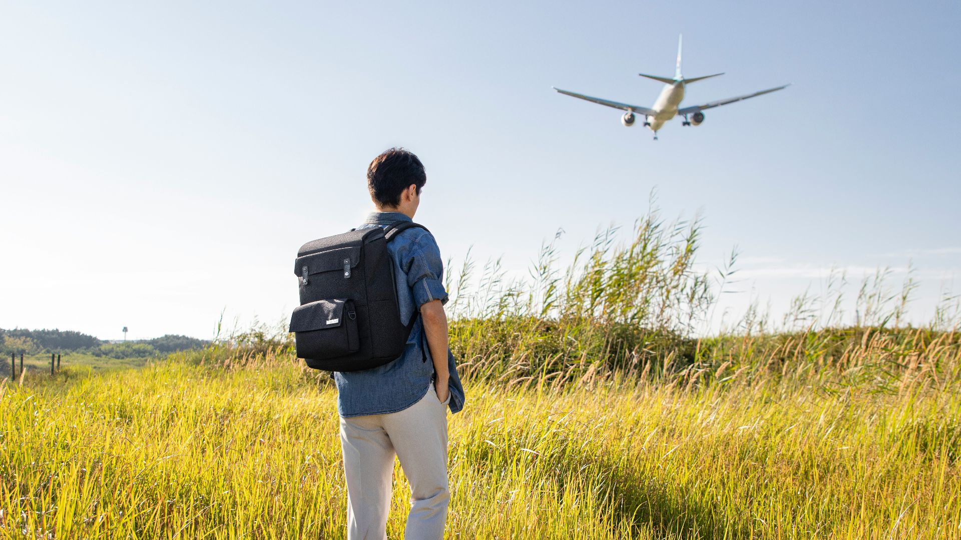 a man with a backpack looking at an airplane in the sky
