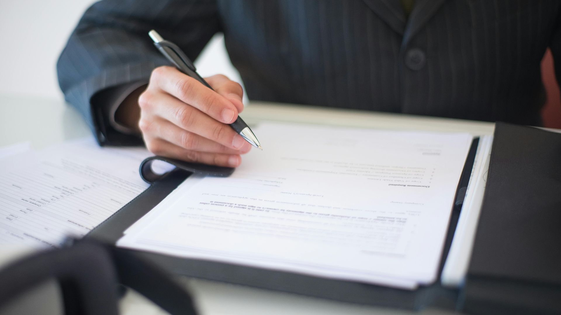 Close-up of a hand signing documents with a pen, symbolizing an important business contract.