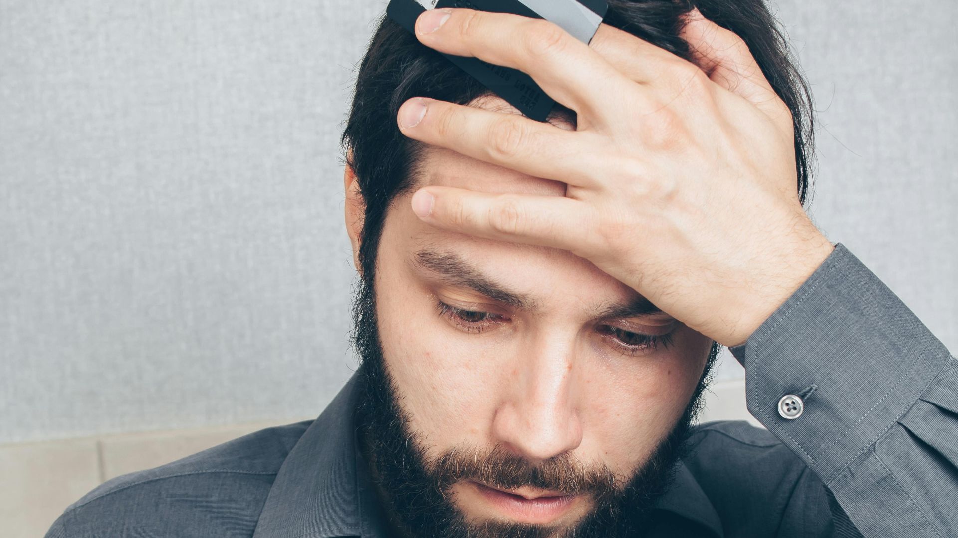 A stressed man looks at his smartphone, holding a credit card in his hand.