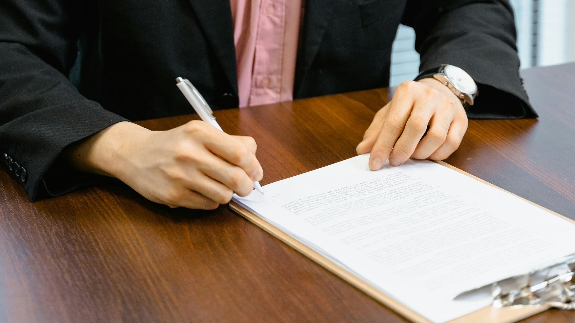 Professional man in business attire signing papers at an office desk.