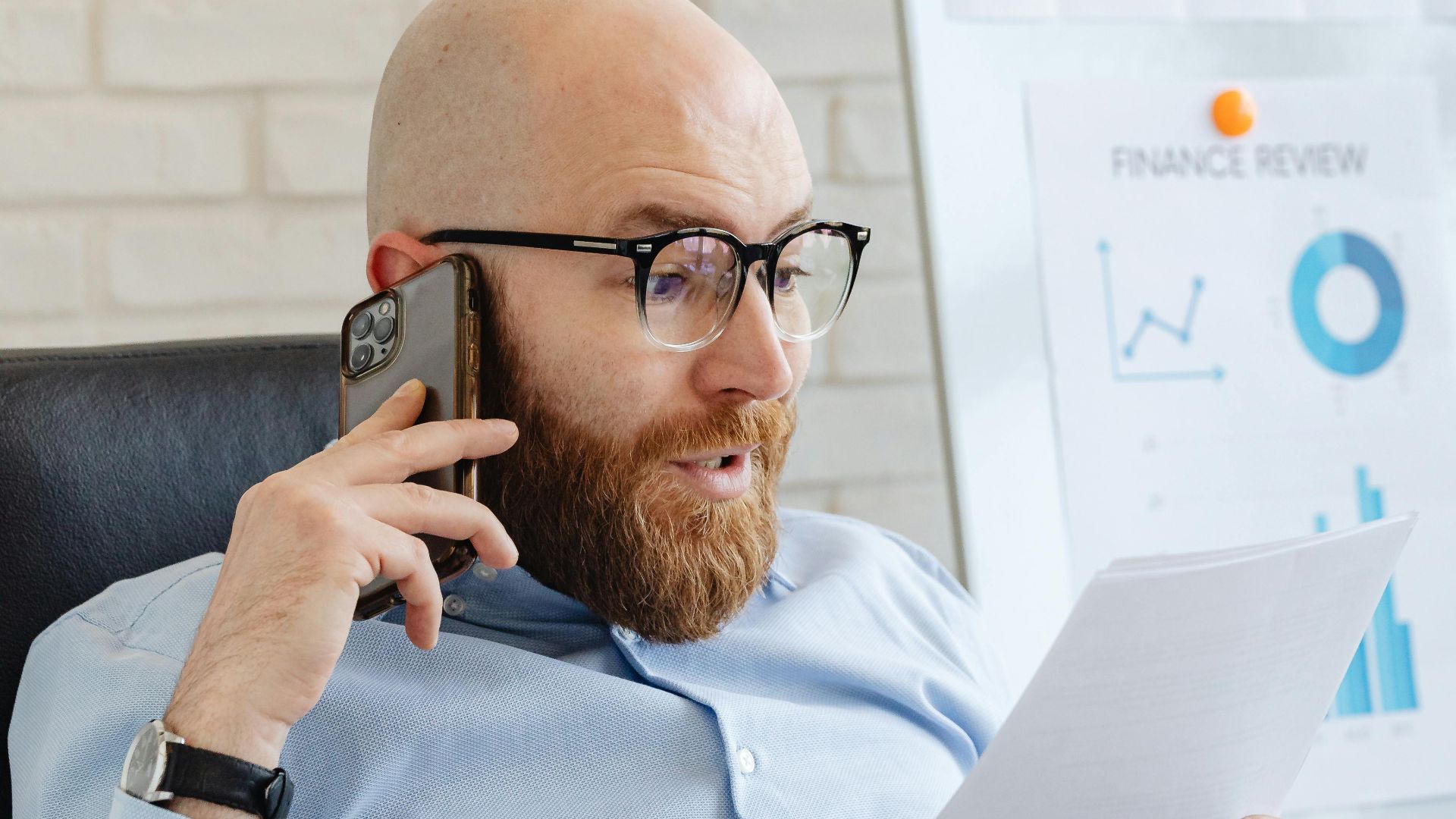 Professional analyzing data charts and graphs on paper and phone in office setting.