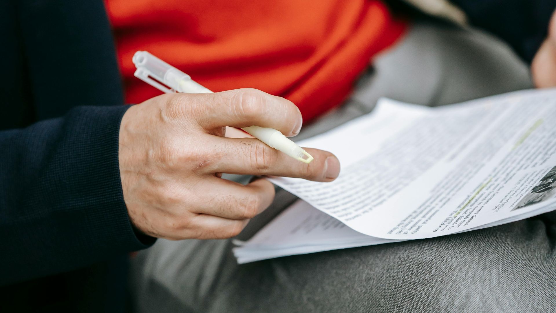 A focused individual reviewing documents outdoors, pen in hand, wearing vibrant clothing.
