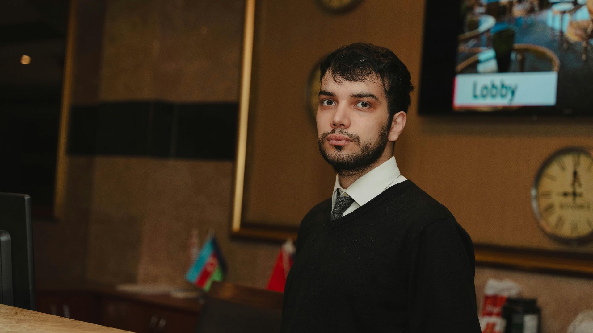A hotel receptionist standing at the front desk in a hotel lobby, ready to assist guests.