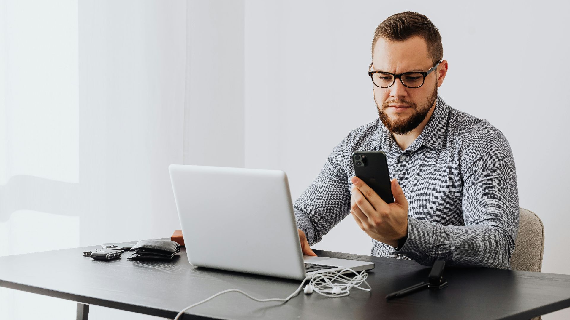 Professional man working at desk with laptop and smartphone, indoors.
