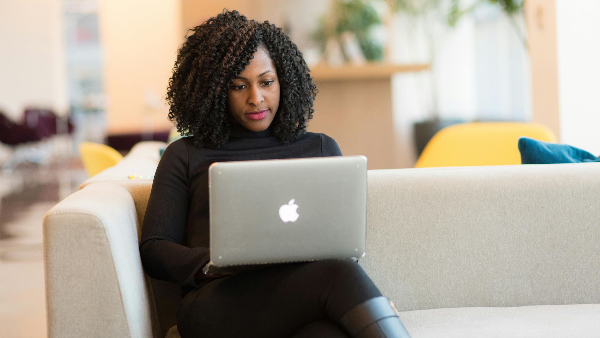 An African American woman working remotely on a laptop in a modern indoor setting.